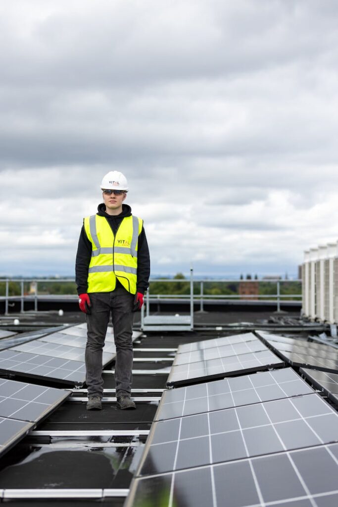 Man in safety vest and helmet inspects rooftop solar panels, promoting renewable energy.